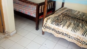 A bedroom with two beds, one with a zebra-patterned bedspread and another with a floral bedspread. There are blue slippers on the floor. - Jordan Guest House (Mai Mahiu)