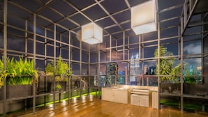 A modern indoor space with a wooden floor, metal grid ceiling, and large windows offering a city view. - Anggun Residence by Sleepy Bear (Kuala Lumpur)