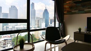 A modern living room with a large window offering a city view, a flat-screen TV, and a wooden accent wall. - Anggun Residence by Sleepy Bear (Kuala Lumpur)