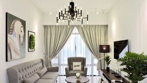 A modern living room with a grey sofa, a round coffee table, a grey armchair, a TV, and a chandelier. - Anggun Residence by Sleepy Bear (Kuala Lumpur)
