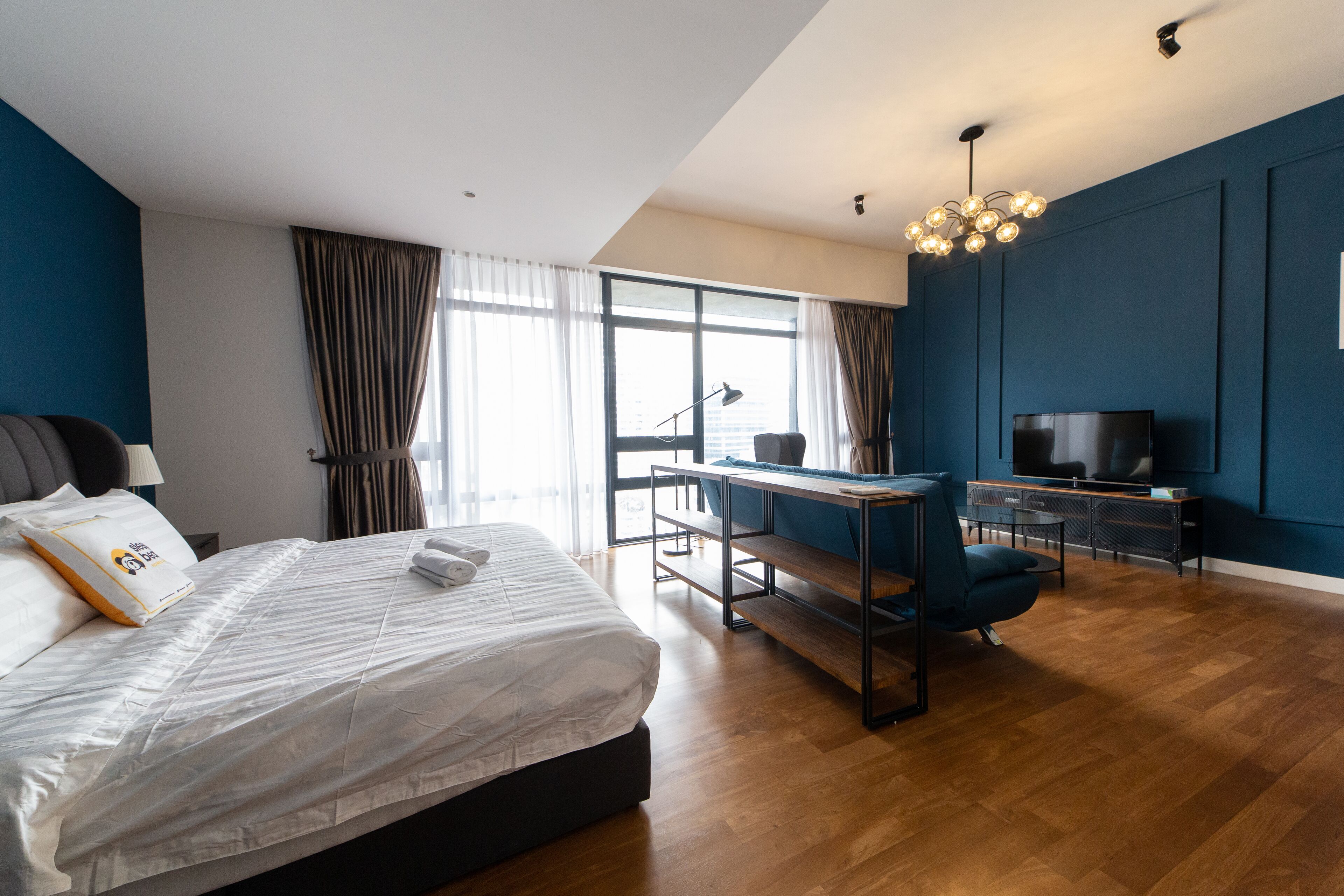 Une chambre d’hôtel moderne, dotée d’un grand lit, d’un bureau avec une chaise, d’une télévision et d’une grande fenêtre avec des rideaux.