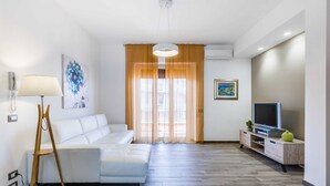 Un salon moderne avec un canapé blanc, un plancher en bois, un téléviseur posé sur un meuble en bois et un tableau accroché au mur.
