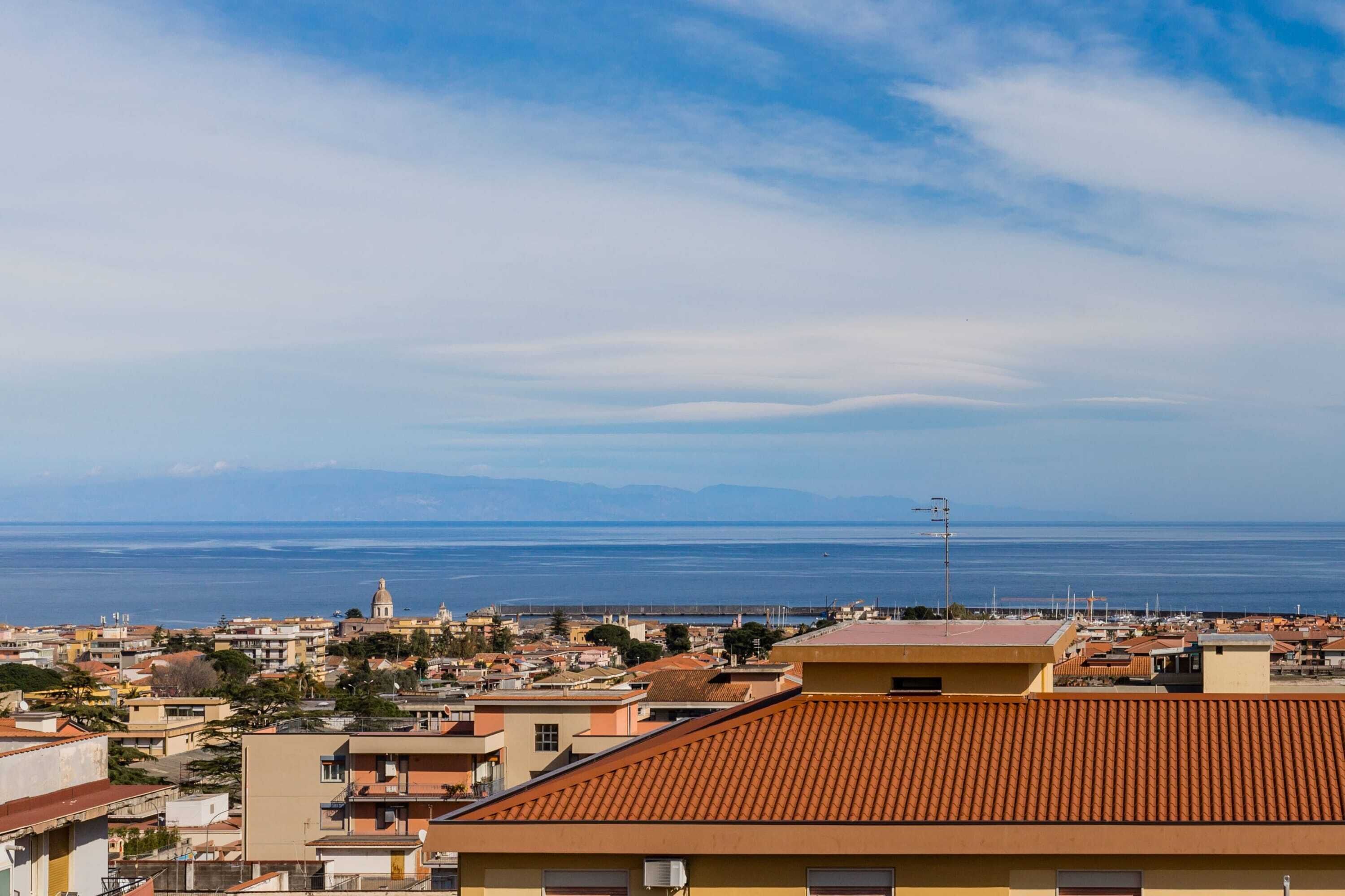 A coastal cityscape with a view of the sea and distant mountains.