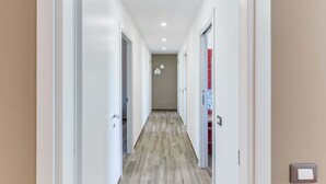 Un couloir moderne avec des murs blancs, un plancher en bois et des spots encastrés au plafond.