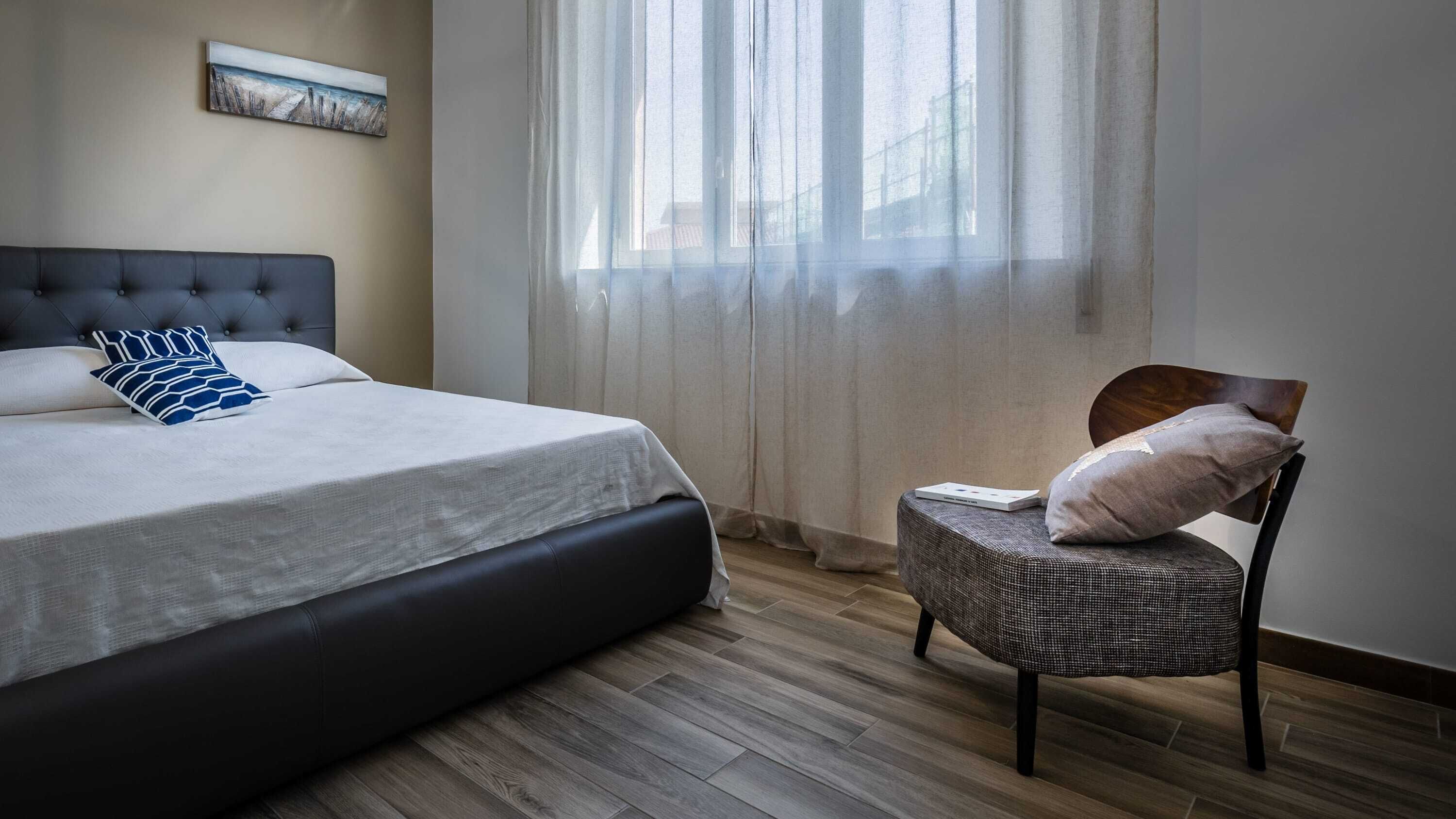 Un dormitori amb un llit, una cadira i una finestra amb cortines.