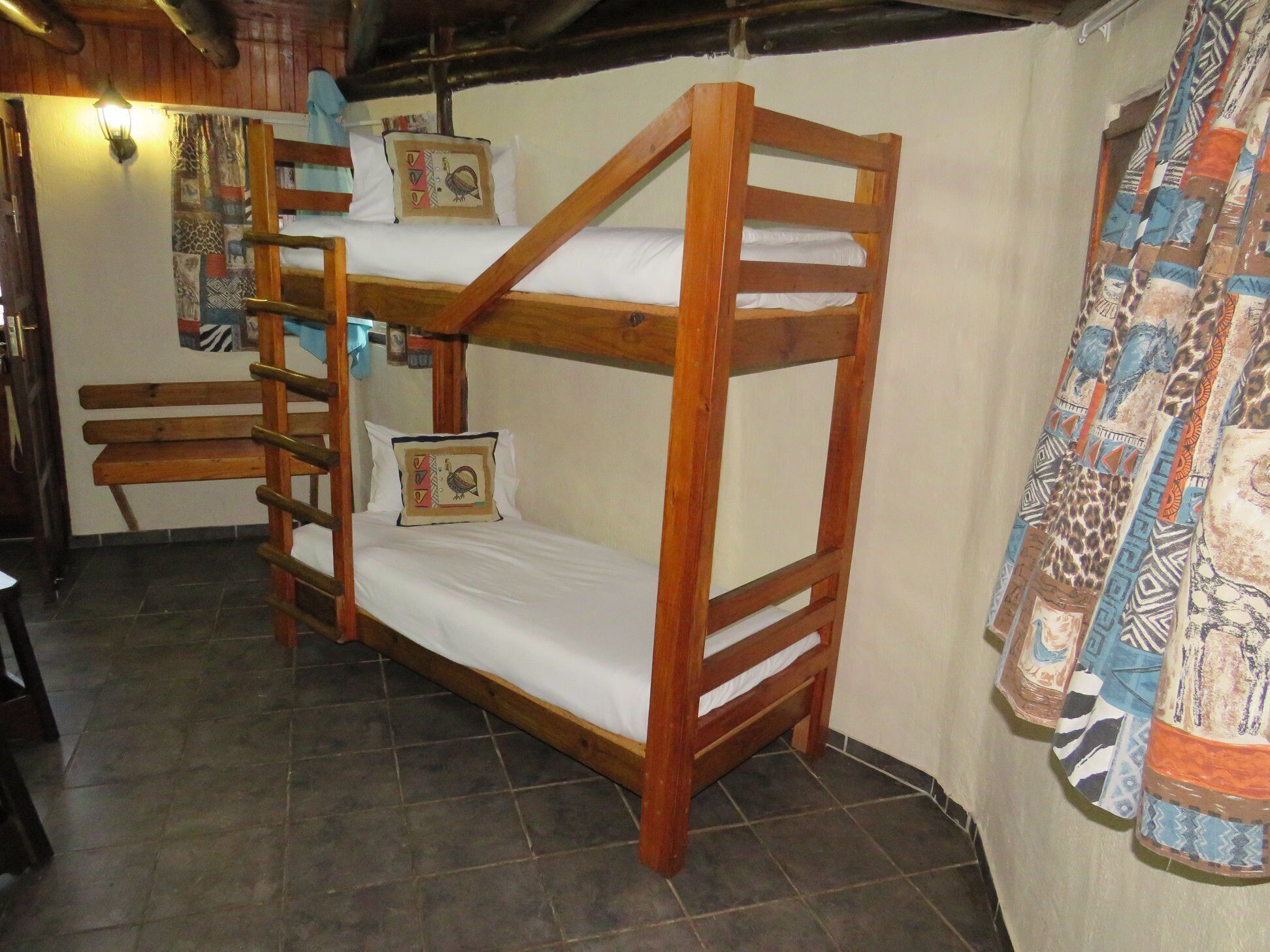 A bunk bed with a ladder, a bench, and a wall with a patterned curtain.