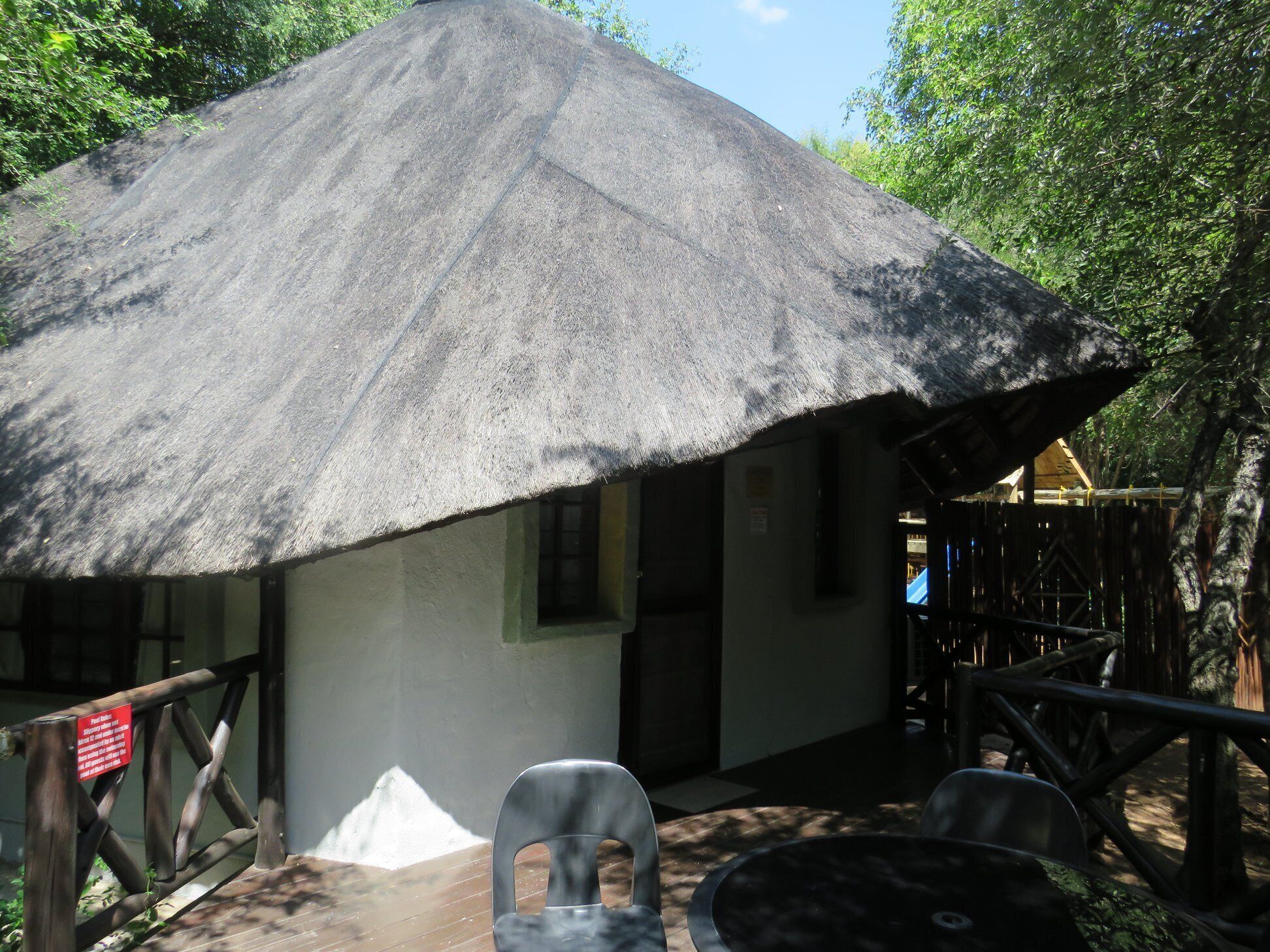 A thatched-roof structure with a wooden deck and outdoor seating.