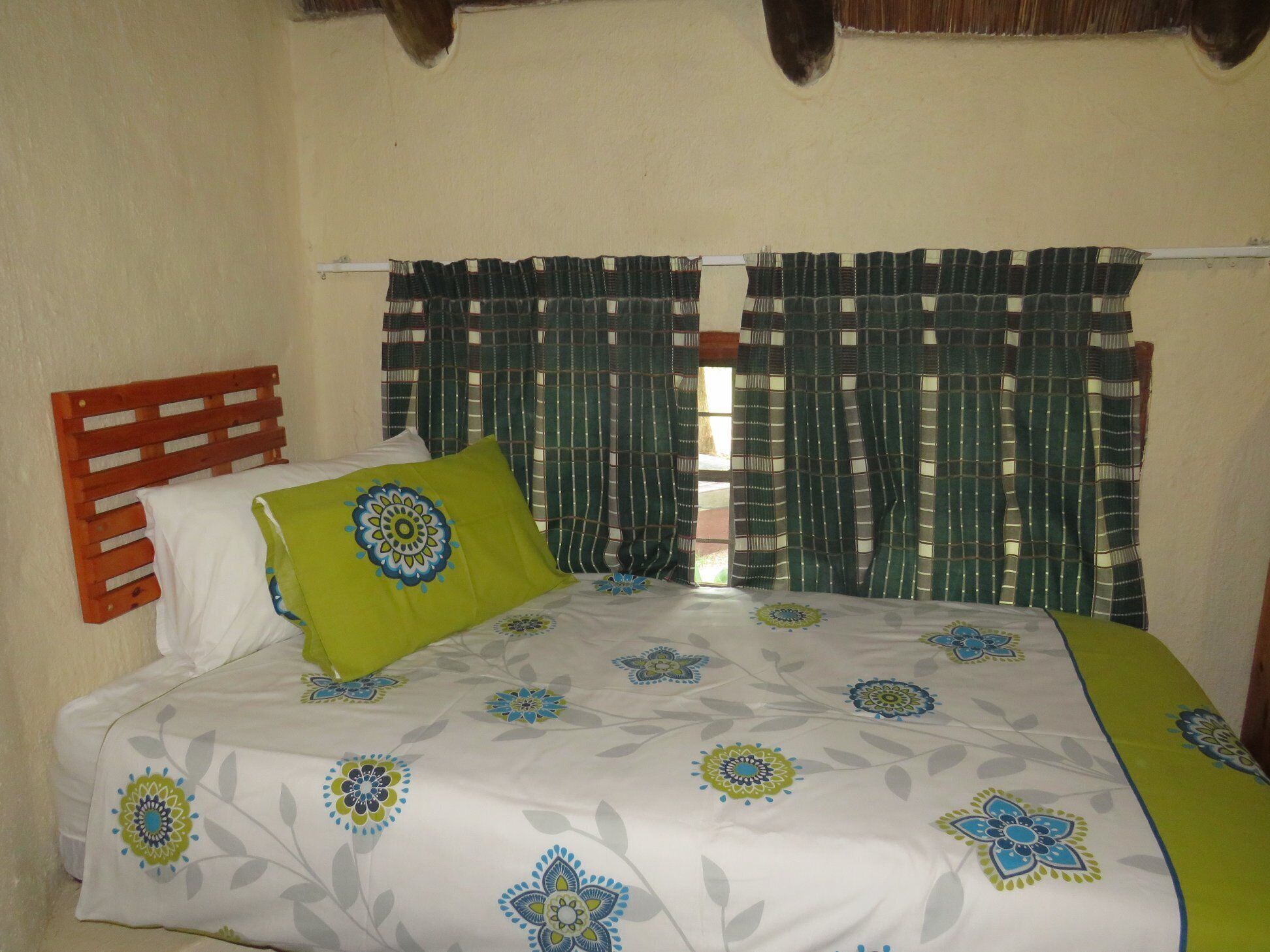 Un lit avec une couvre-lit à motifs floraux, un oreiller vert et une tête de lit en bois.