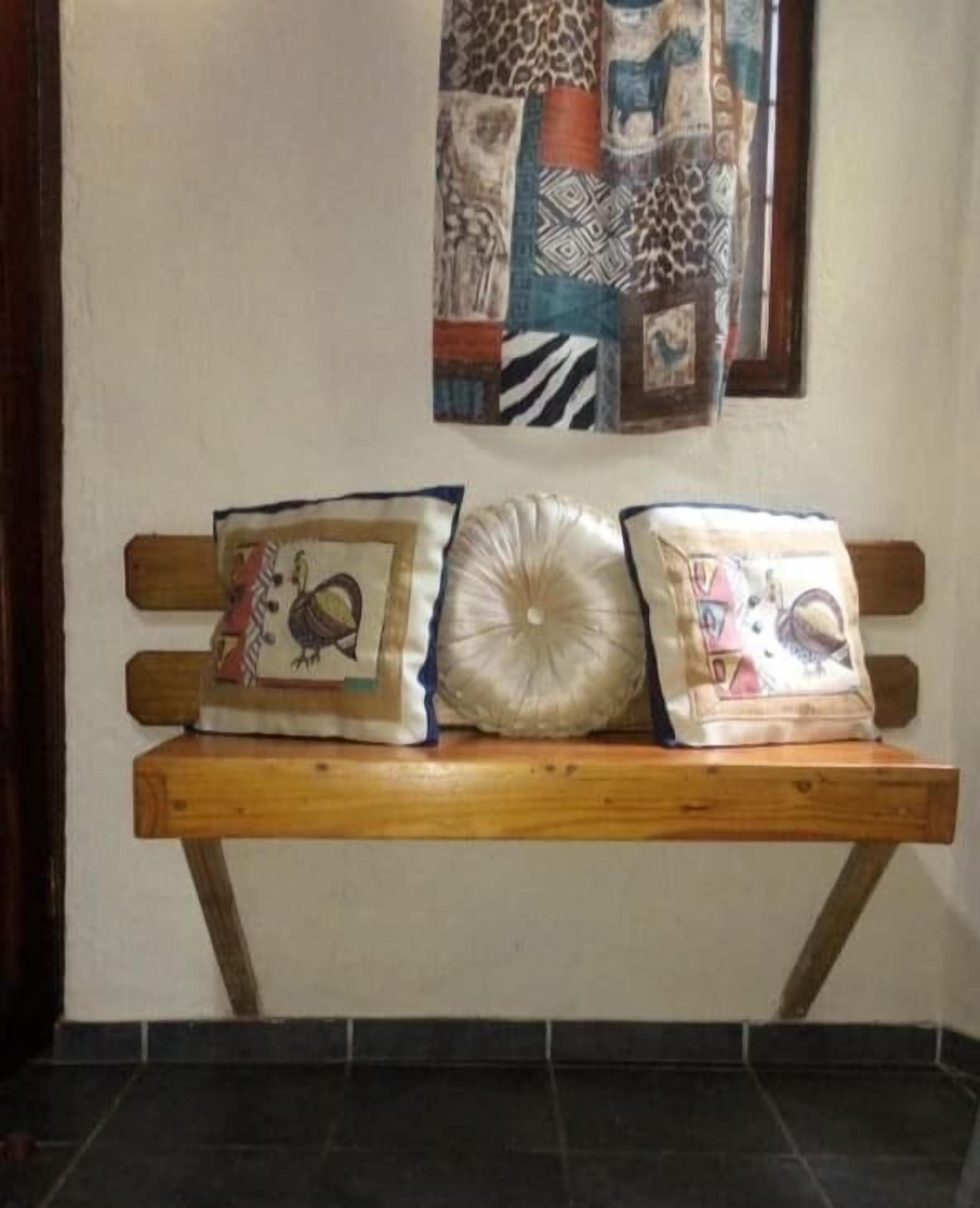 A wooden bench with two pillows against a wall, one with a bird design and the other with a floral pattern.