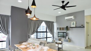 Un espace repas moderne avec une table en bois pouvant accueillir six personnes, des chaises à revêtement gris, un éclairage suspendu et un ventilateur de plafond.