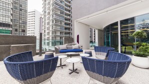 Un espace extérieur moderne aménagé avec des meubles en osier et un canapé bleu, entouré de grands immebles.