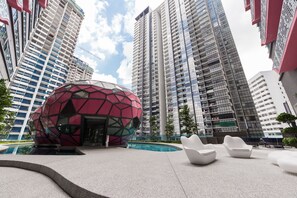 A modern building with a unique spherical structure, surrounded by high-rise apartments and a pool area.
