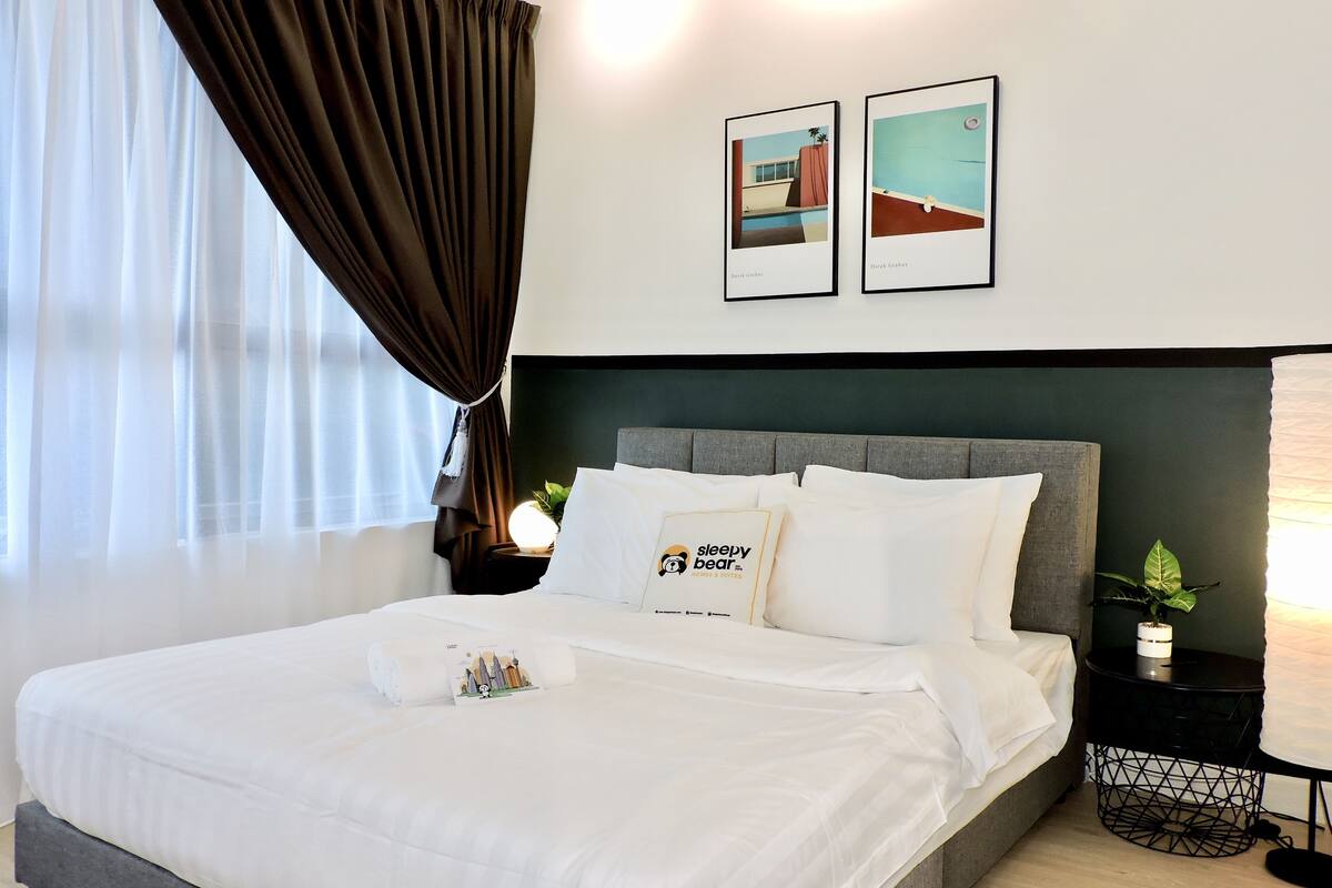 A neatly made bed with white linens and a pillow with a bear logo, a dark headboard, and two framed pictures on the wall.