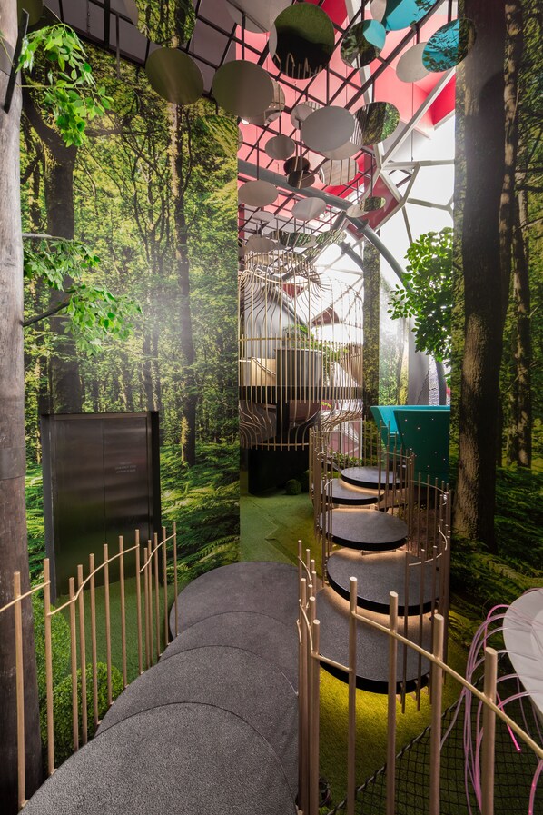 A modern indoor space with a forest-themed mural, a spiral staircase, and seating areas.