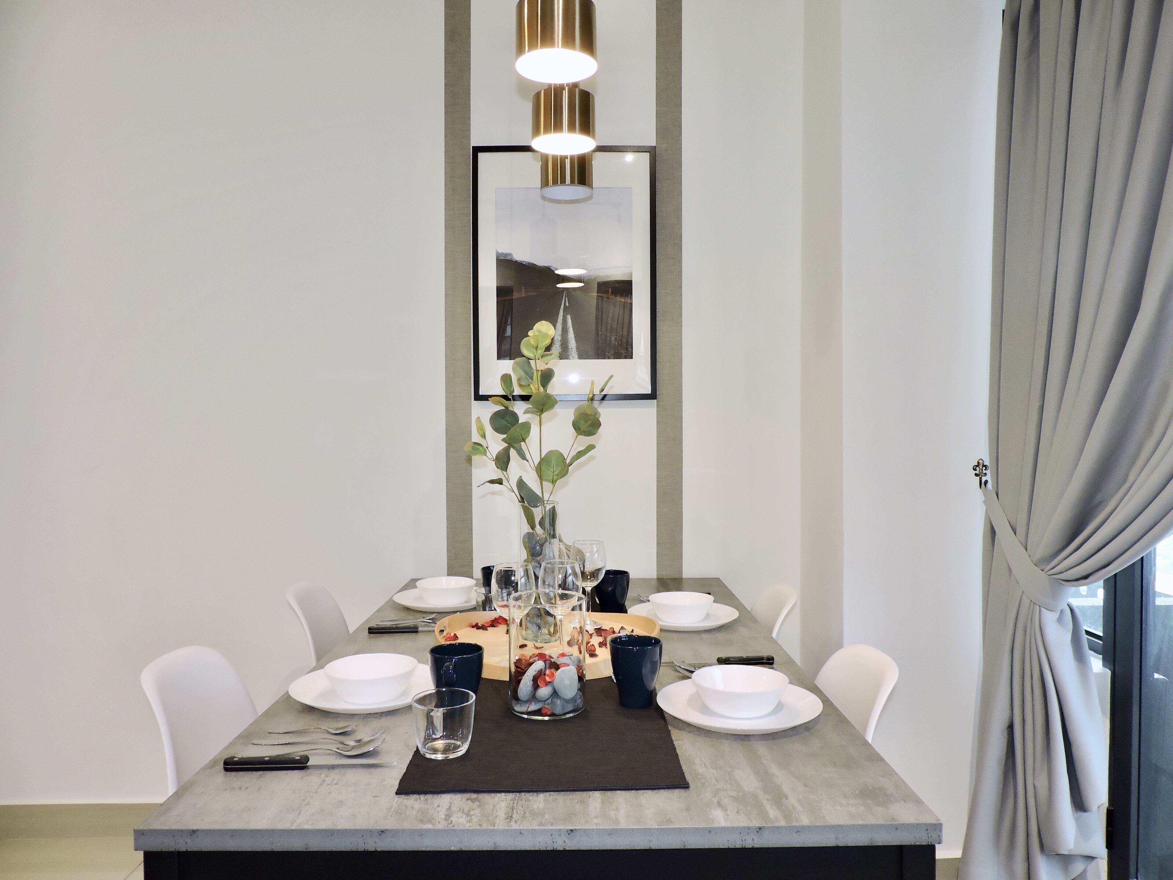 A modern dining area with a marble table, white chairs, a vase with green foliage, and a framed picture on the wall.