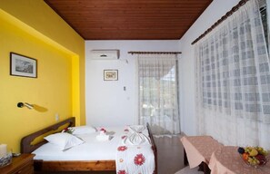 Ein Schlafzimmer mit einem Bett, einem Nachttisch, einem Tisch mit Früchten und einem Fenster mit Vorhängen.
