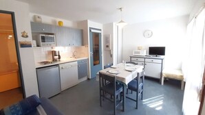 Une cuisine compacte avec un coin repas, un canapé, un téléviseur et une horloge au mur.
