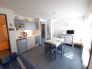 Kompakti keittiö, jossa on ruokailutila, sohva, televisio ja seinällä oleva kello.