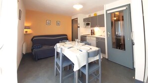 Un espace de vie compact comprenant un coin cuisine, une table à manger avec des chaises, un canapé et une porte donnant accès à la salle de bain.