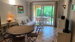 A cozy room with a round dining table, a sofa, and a TV. - 3-room apartment with large private garden, air conditioning and parking (Cavalaire-sur-Mer)