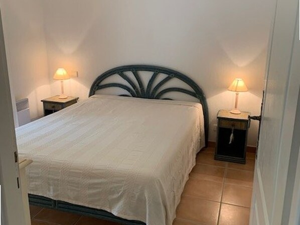 Un dormitorio con una cama, dos mesitas de noche con lámparas y suelo de baldosas.