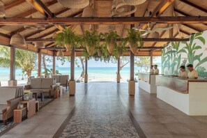 Un espace de réception situé au bord de la plage, doté d’un toit de chaume, de jardinières suspendues et offrant une vue sur la mer.