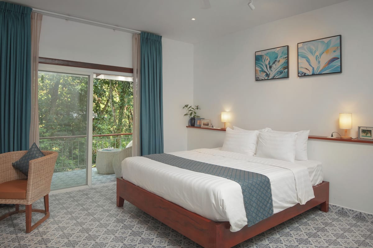A bedroom with a large bed, a chair, a balcony with curtains, and two wall-mounted lamps.