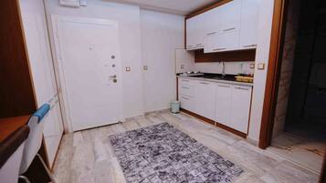 Una cucina compatta con mobili bianchi, pavimento piastrellato e tappeto decorativo.