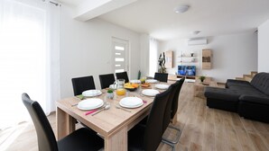 Een moderne eetruimte met een houten tafel gedekt voor vier personen, zwarte stoelen en een zwarte bank achterin.