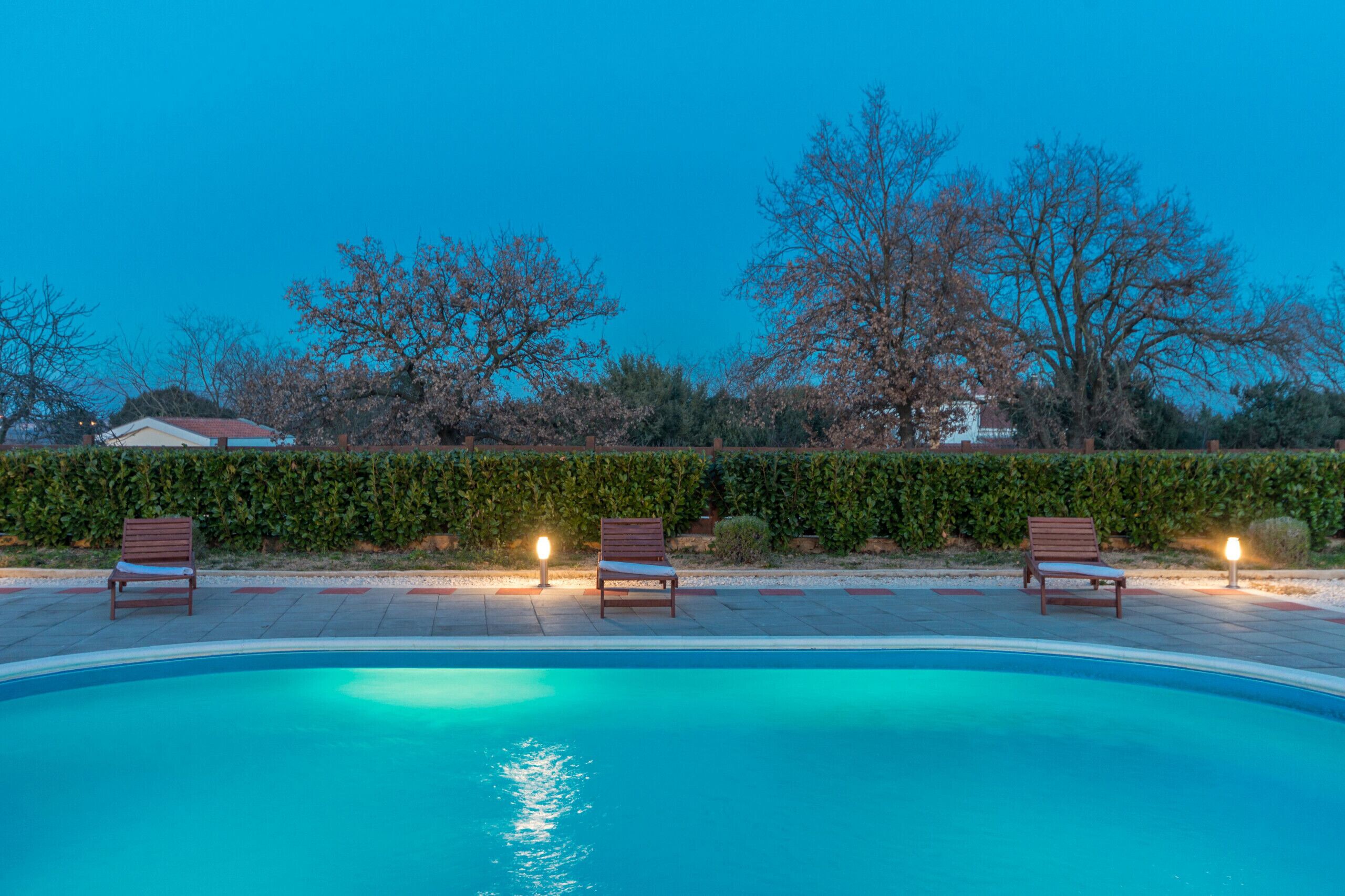 Ein Swimmingpool mit drei Holzliegen und Beleuchtung am Rand.