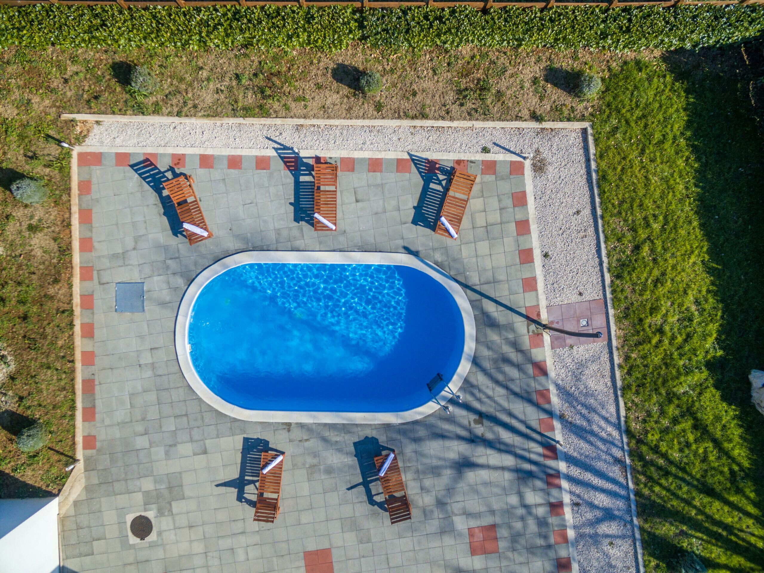 An aerial view of a swimming pool area with a tiled deck, surrounded by lounge chairs and a small pool.