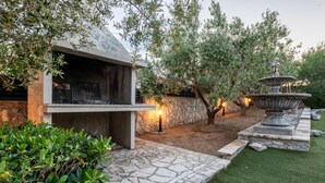 An outdoor patio area with a stone grill, a fountain, and a well-maintained lawn. - Villa Elder (Benkovac)