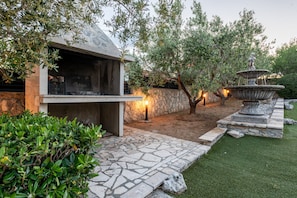 An outdoor patio area with a stone grill, a fountain, and a well-maintained lawn. - Villa Elder (Benkovac)