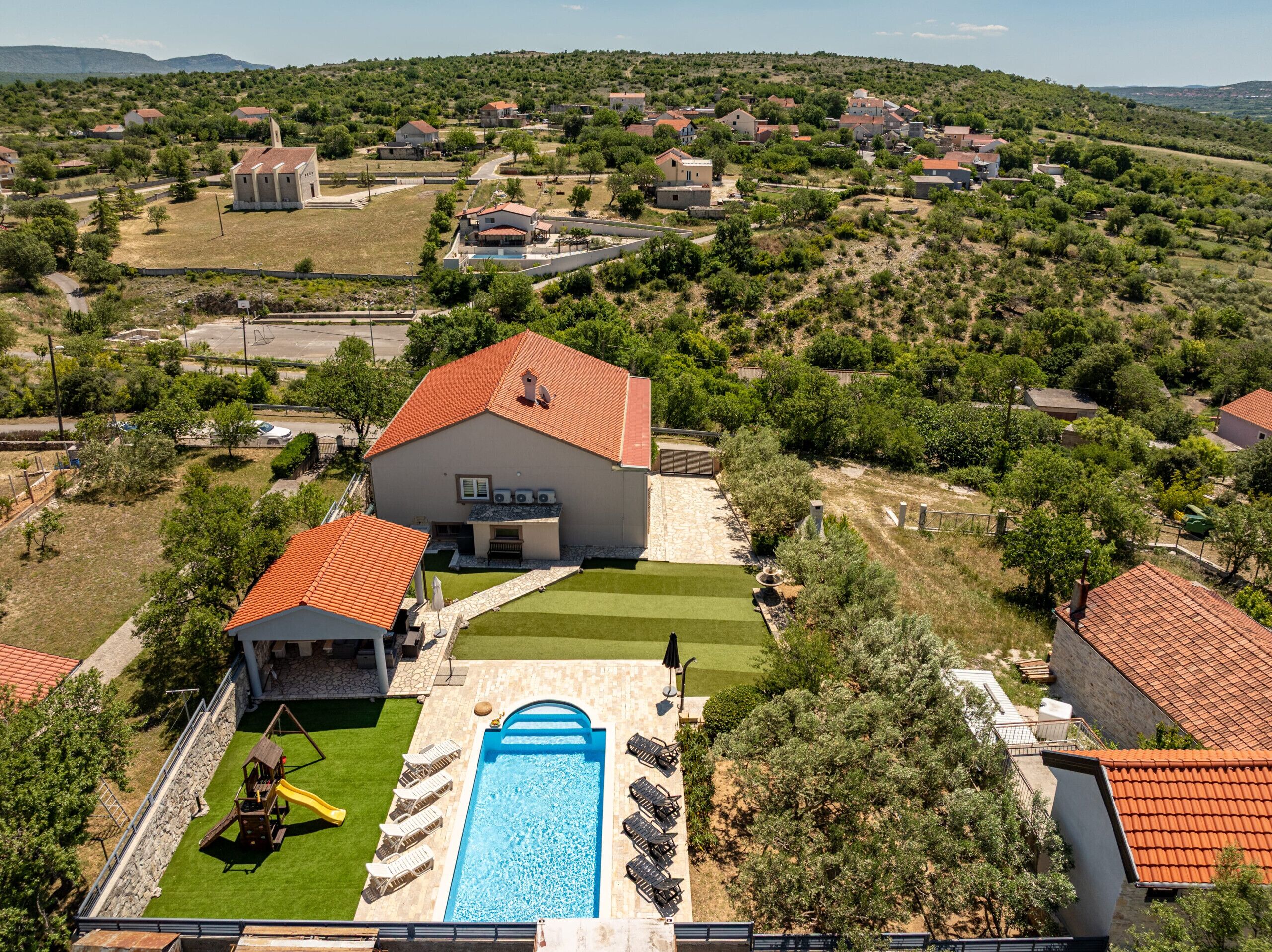 A residential area with a large house featuring a swimming pool, a patio, and a playground.