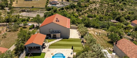 Un barrio residencial con una casa grande que tiene piscina, patio y parque infantil.