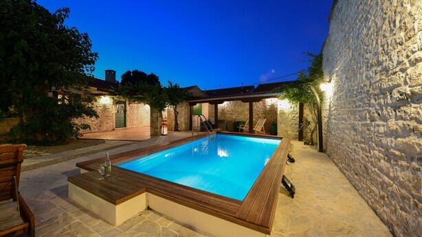 A rectangular swimming pool with a wooden deck, surrounded by stone walls and a stone floor. - Villa Oak (Benkovac)