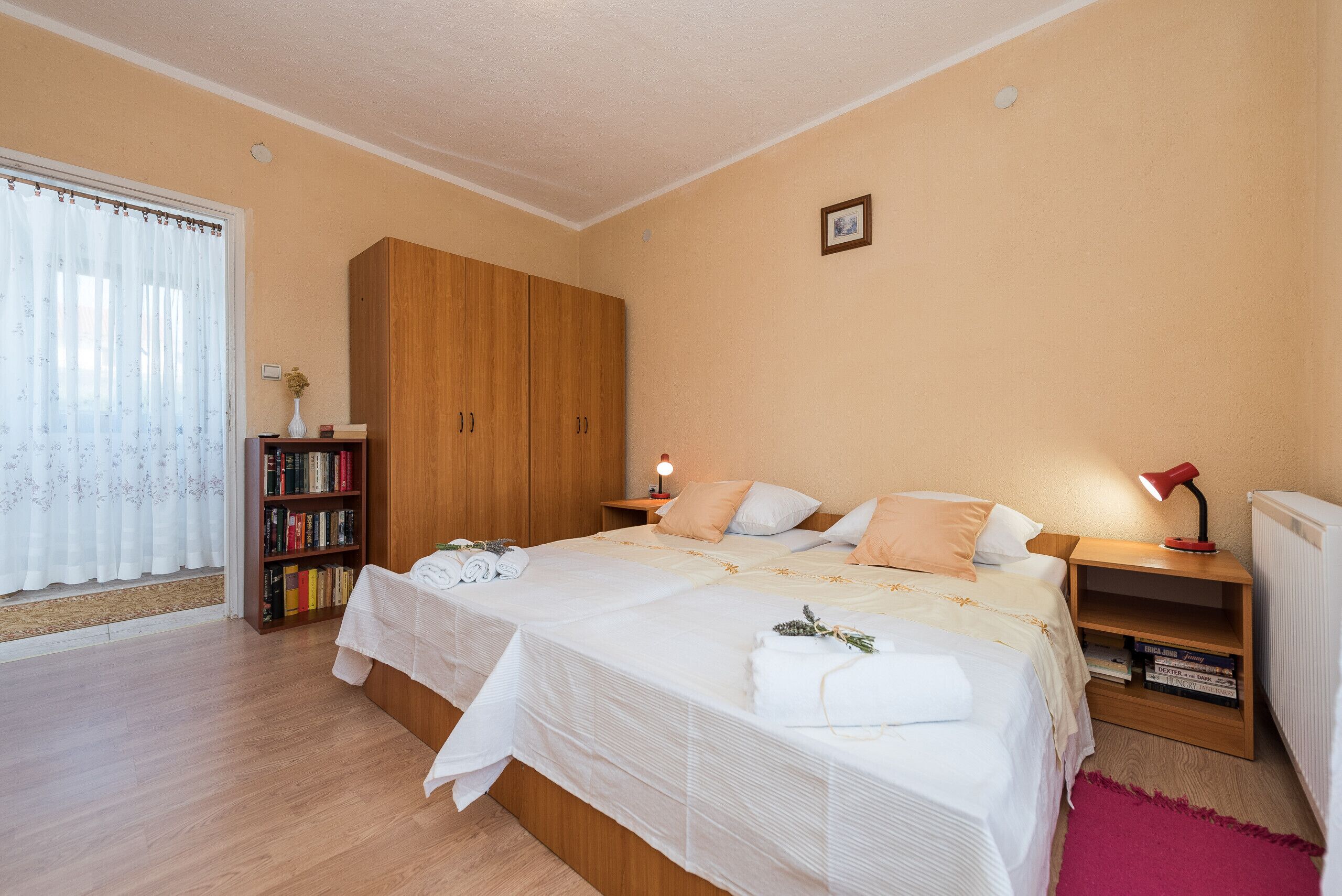 Une chambre avec deux lits, une armoire en bois, une bibliothèque et une table de chevet avec une lampe.