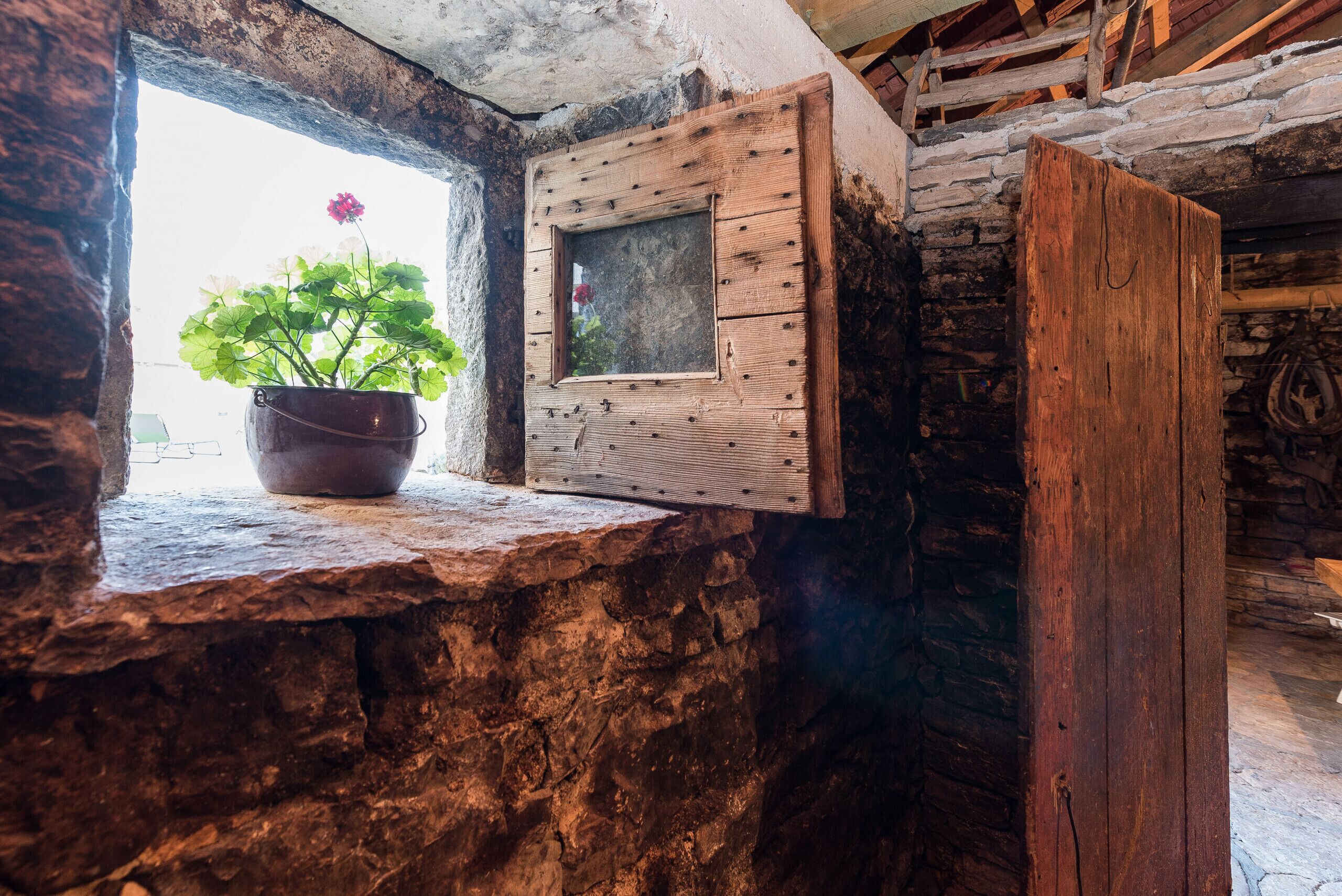 A rustic stone wall with a wooden window frame and a potted plant.