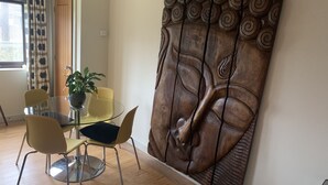A dining area with a glass table, four chairs, a potted plant, and a large wooden wall art piece. - King Canute Apartment - Crown Lettings (Chichester)