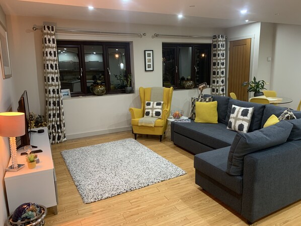 Una sala de estar moderna con un sofá, un sillón y una mesita de noche con una lámpara.