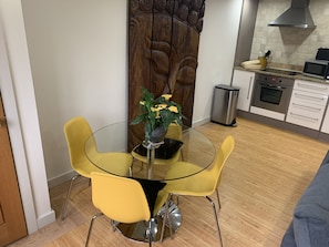 A modern kitchen with a dining area featuring a glass table and yellow chairs.