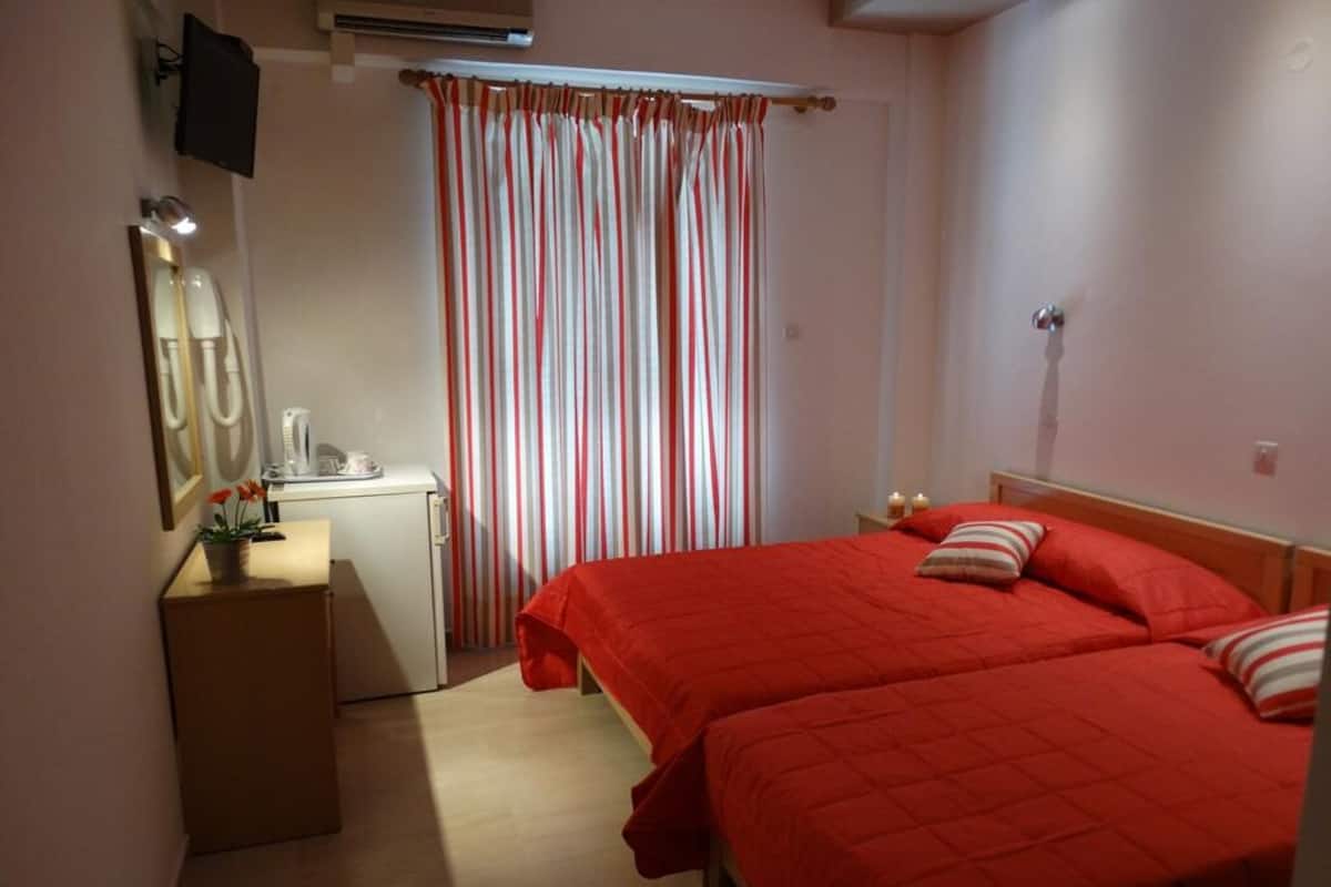 A bedroom with two beds, a bedside table, a mirror, a telephone, and a curtain.