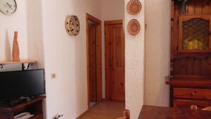 Una stanza con un tavolo da pranzo in legno, un televisore su un mobile, un armadio in legno e una porta che dà su un'altra stanza.