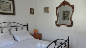 Un letto rifatto con lenzuola bianche e asciugamani arrotolati, un comodino in legno con una lampada e un grande specchio appeso al muro.