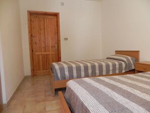 A bedroom with two single beds, a wooden wardrobe, and a small bedside table.