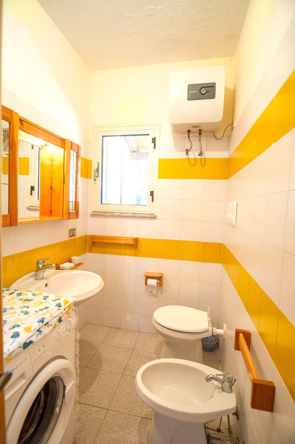 A compact bathroom with a washing machine, two sinks, a toilet, and a window.