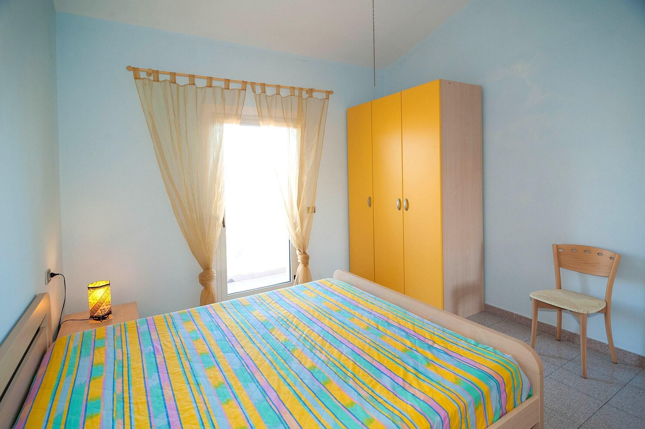 Un dormitorio con cama, armario, silla y mesita de noche con lámpara.