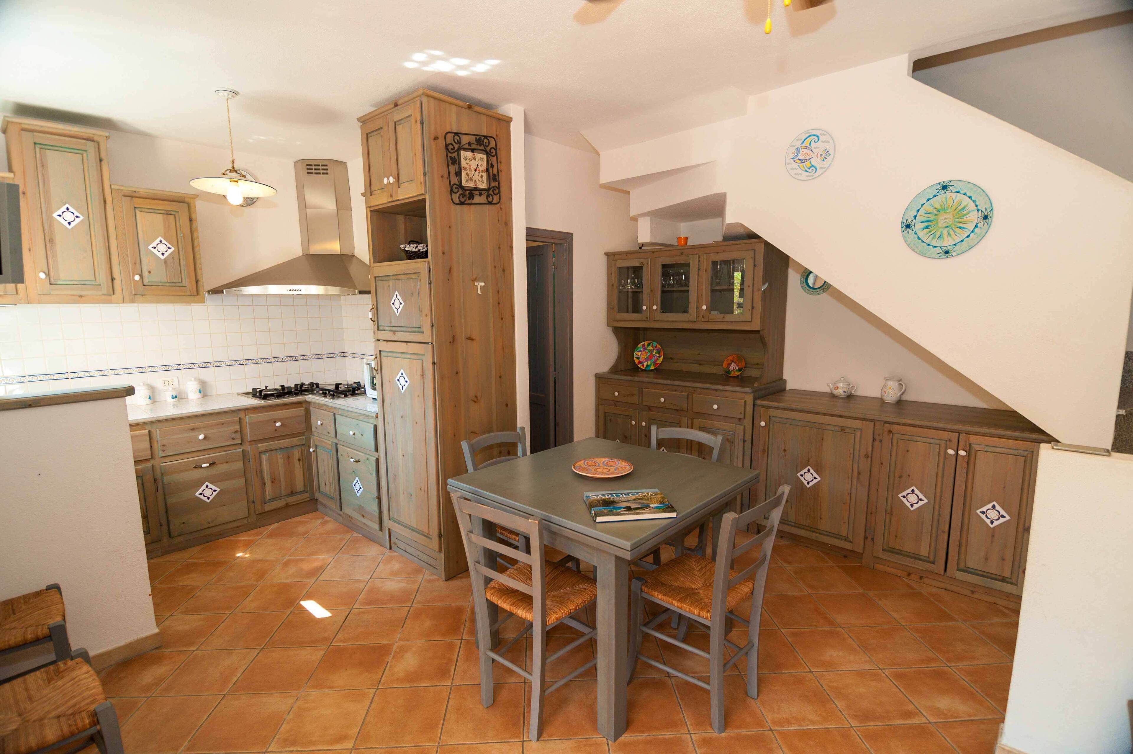Una cocina con armarios de madera, una mesa de comedor con sillas y piso de baldosas.