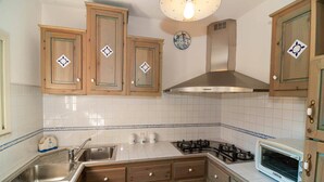 Una cocina con armarios de madera, estufa a gas, lavamanos y microondas.