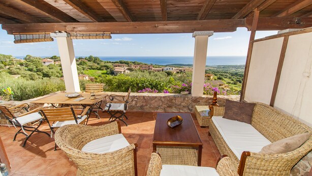 A covered outdoor seating area with wicker furniture, a table, and a view of the sea and surrounding landscape. - Fantastic Sardinia Casa Castas cast01 (Budoni)